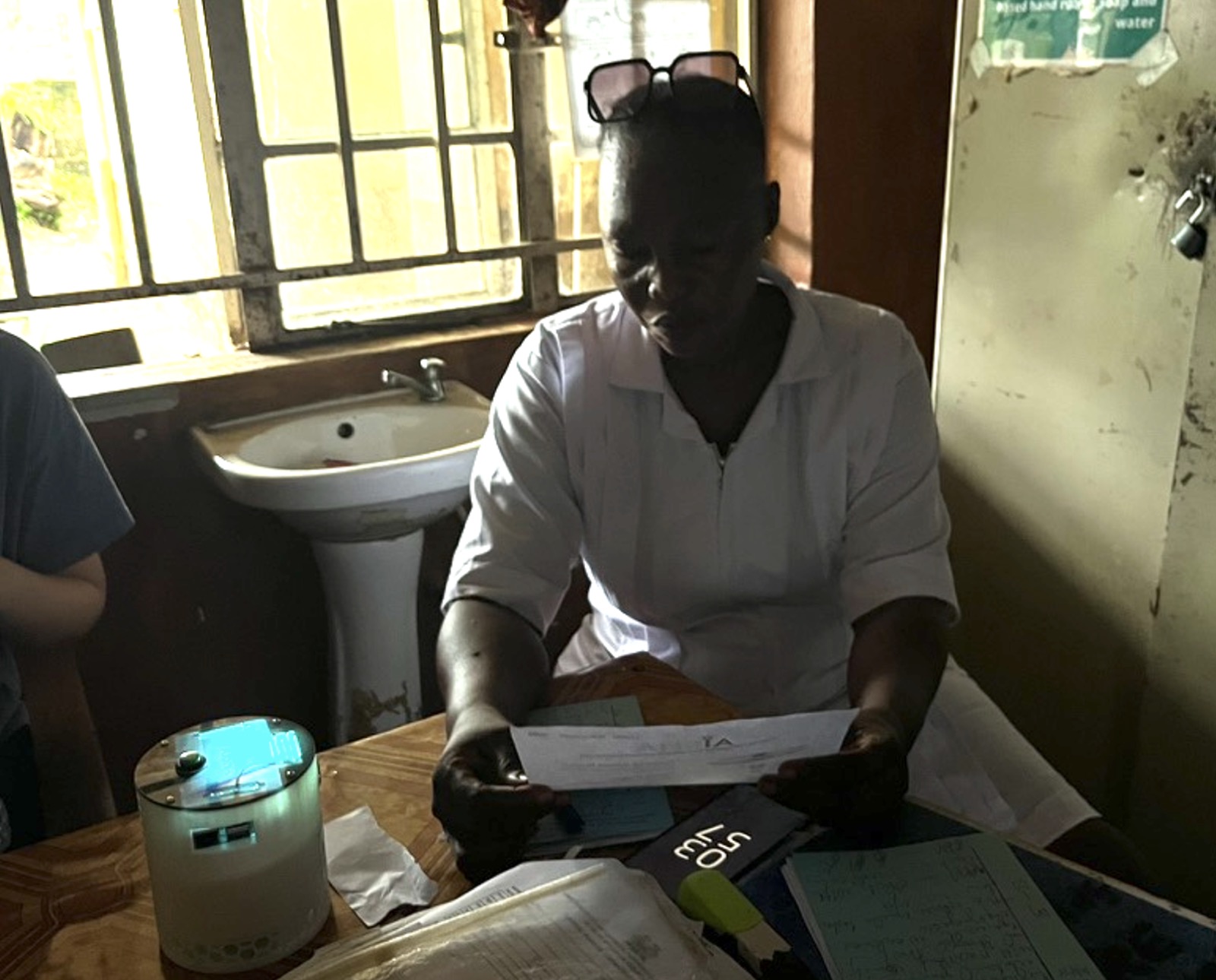 A health worker at a desk in a rural clinic with an AISHA device beside her paperwork