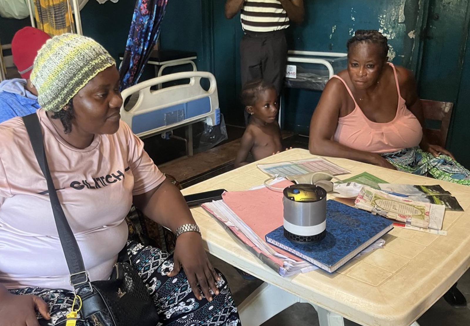 Health workers and patients around a table at a rural clinic with an AISHA device in the middle
